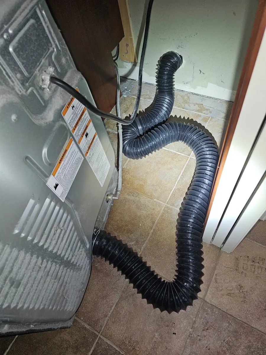 Technician on a ladder cleaning a second floor dryer vent
