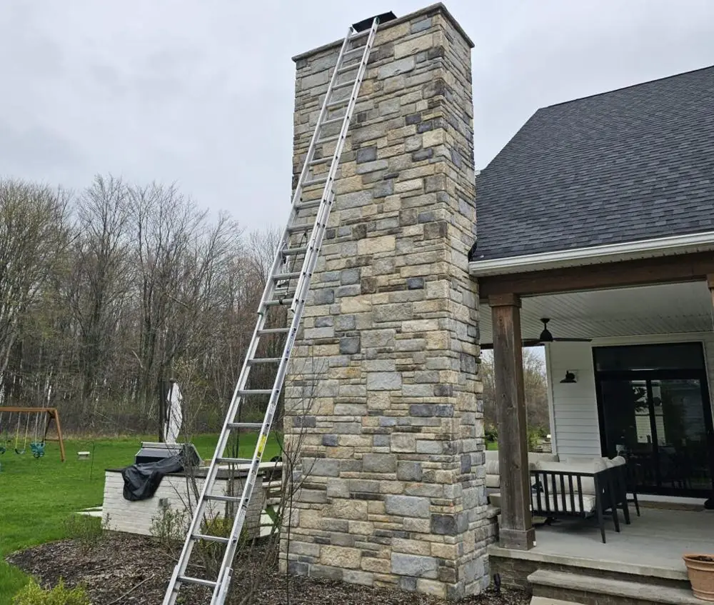 Ladder set against a stone chimney for a fireplace and flue inspection